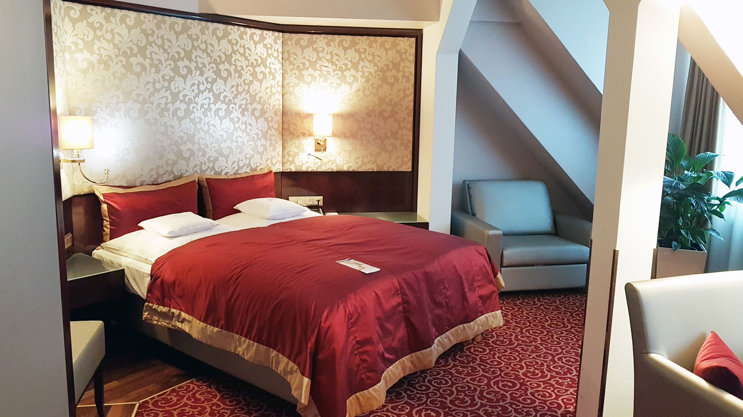 A hotel room with a large bed, two bedside lamps, a chair, and a small table.