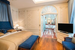 A hotel room with a large bed, a television, a seating area, and a bathroom visible through an arched doorway. - Best Western Plus Hotel StadtPalais (Braunschweig)