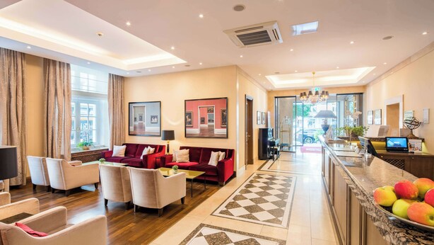 A spacious hotel lobby with a red sofa, multiple armchairs, a coffee table, and a checkered floor pattern. - Best Western Plus Hotel StadtPalais (Braunschweig)