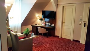 A hotel room with a desk, a chair, a TV, a door, and a red patterned carpet. - Best Western Plus Hotel StadtPalais (Braunschweig)