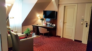 A hotel room with a desk, a chair, a TV, a door, and a red patterned carpet. - Best Western Plus Hotel StadtPalais (Braunschweig)
