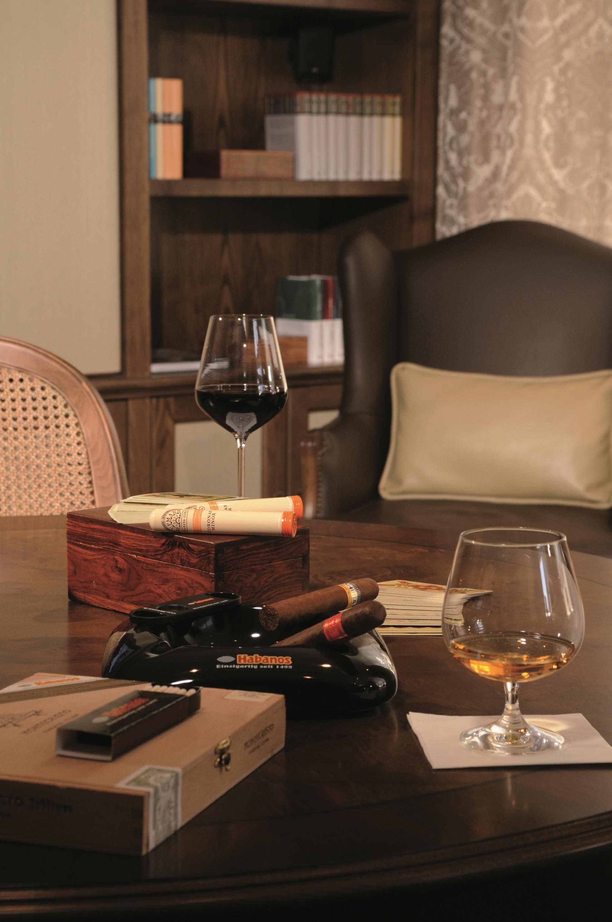 A wooden table with a glass of wine, a cigar, and a cigar box.