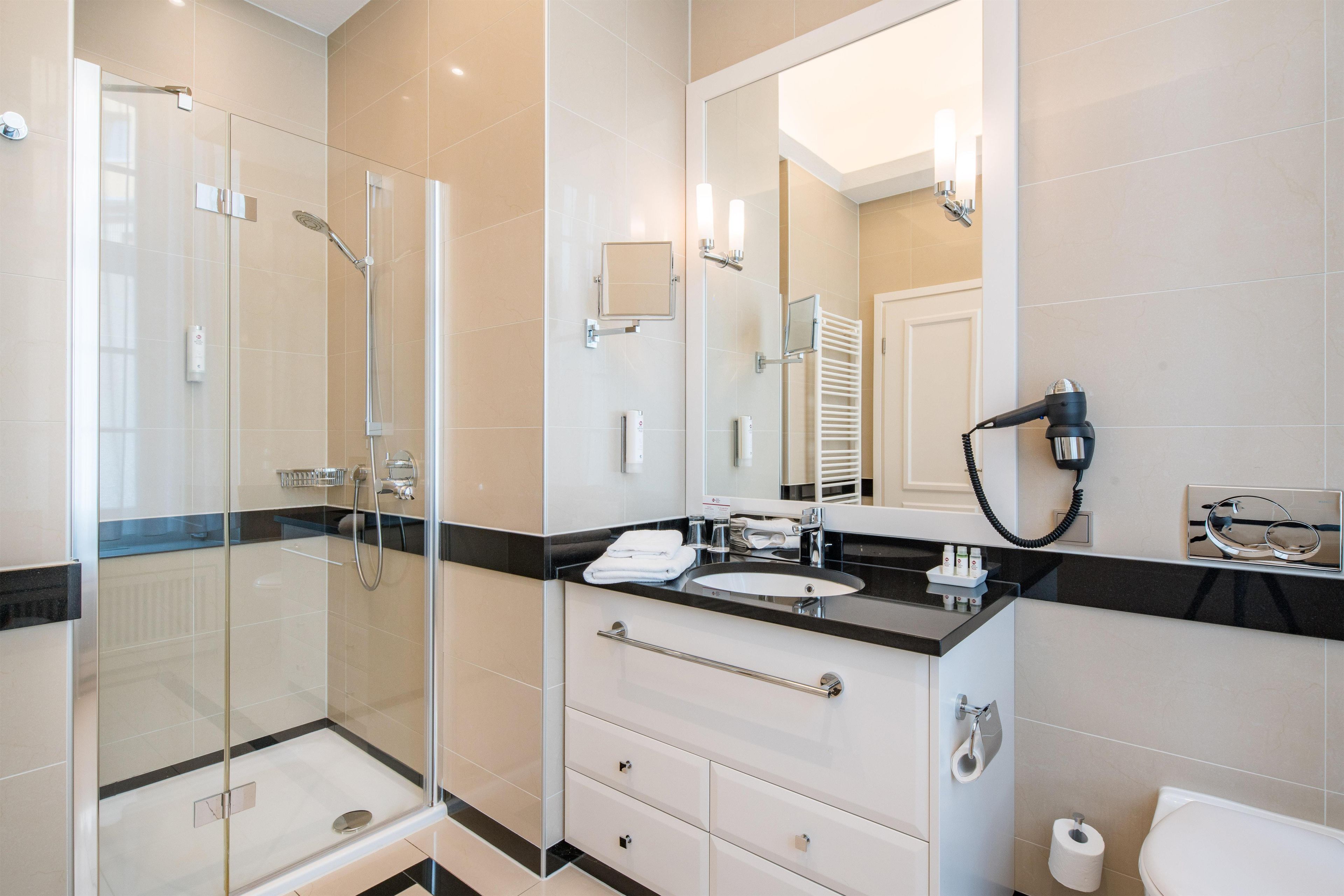A modern bathroom with a glass-enclosed shower, a vanity with a black countertop, and a large mirror.