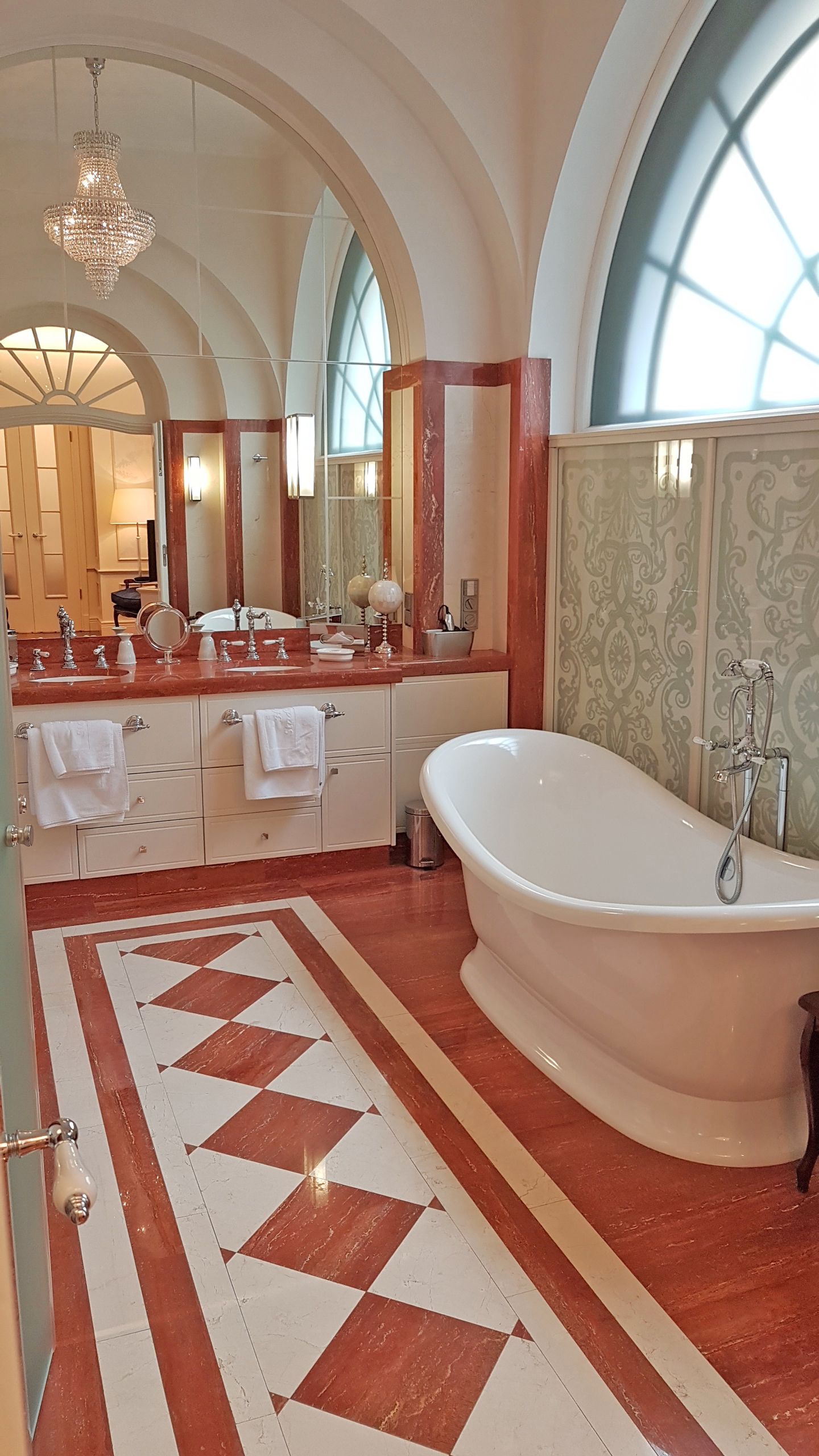 A luxurious bathroom with a large freestanding bathtub, a double vanity with a mirror, and a chandelier.