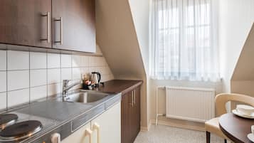 Una cocina con pileta, estufa y alacenas, una ventana con cortinas, y un comedor con una silla y mesa.