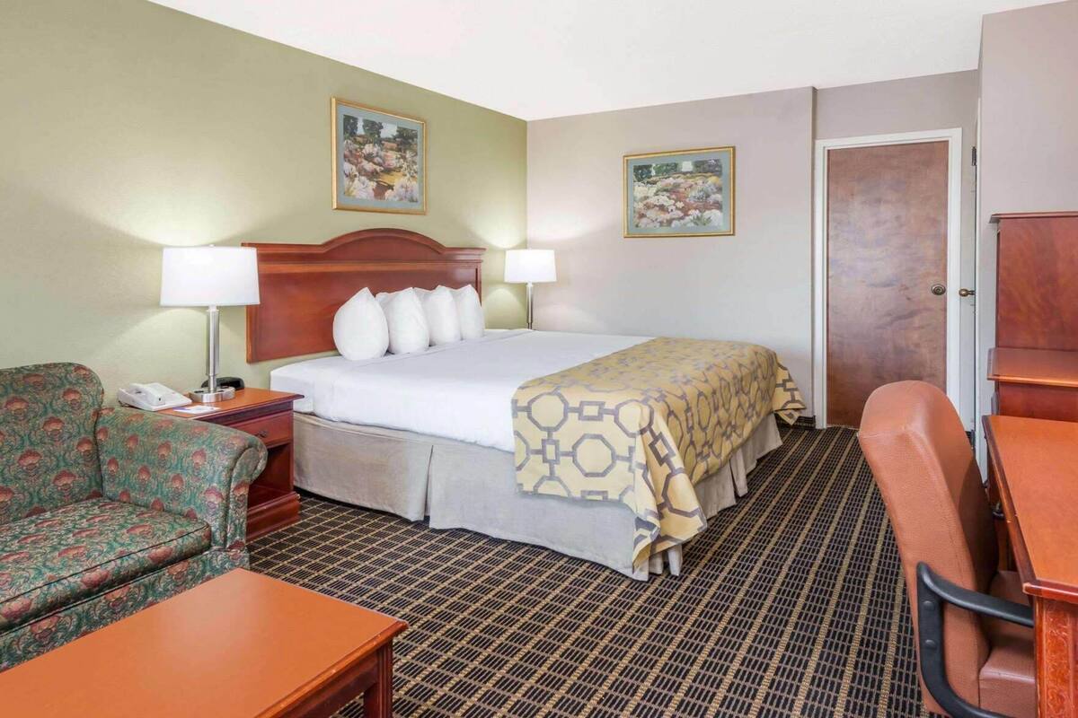 Une chambre d’hôtel comprenant un lit, deux chaises, un bureau, une table de chevet et deux lampes fixées au mur.