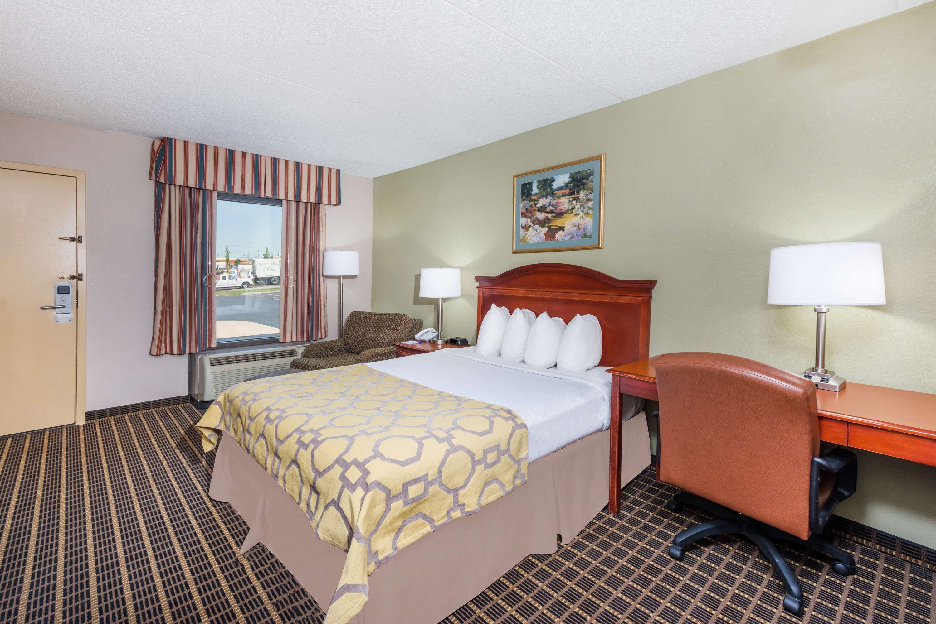 Quarto de hotel com cama, escrivaninha, cadeira e janela com cortinas.