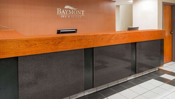 A reception desk with a wooden top and dark panels, featuring the Baymont Inn & Suites logo. - Baymont by Wyndham Clarksville Northeast (Clarksville)