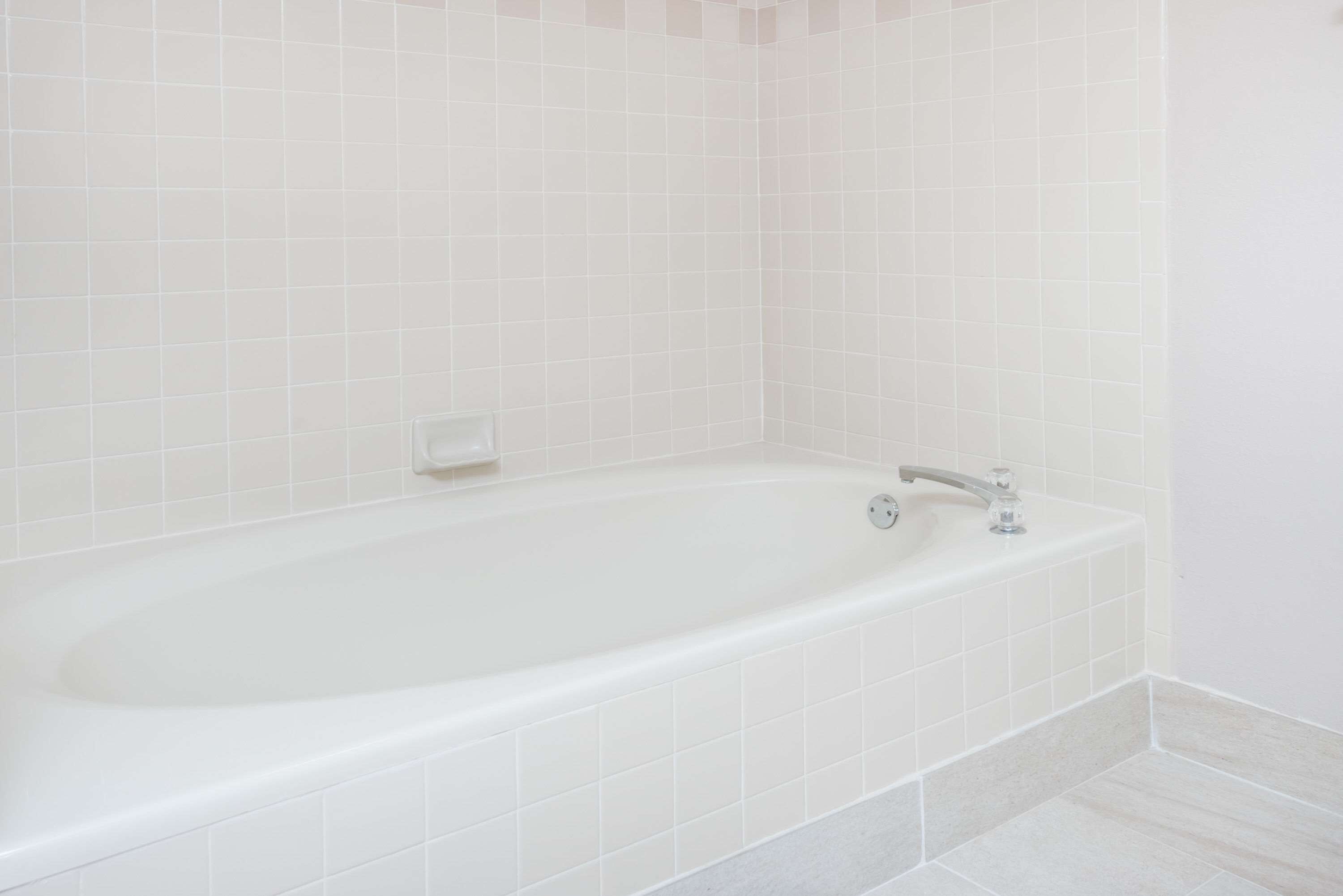 Une baignoire blanche, dotée d’un seul robinet et d’un porte-savon, placée devant un mur recouvert de carreaux simples.