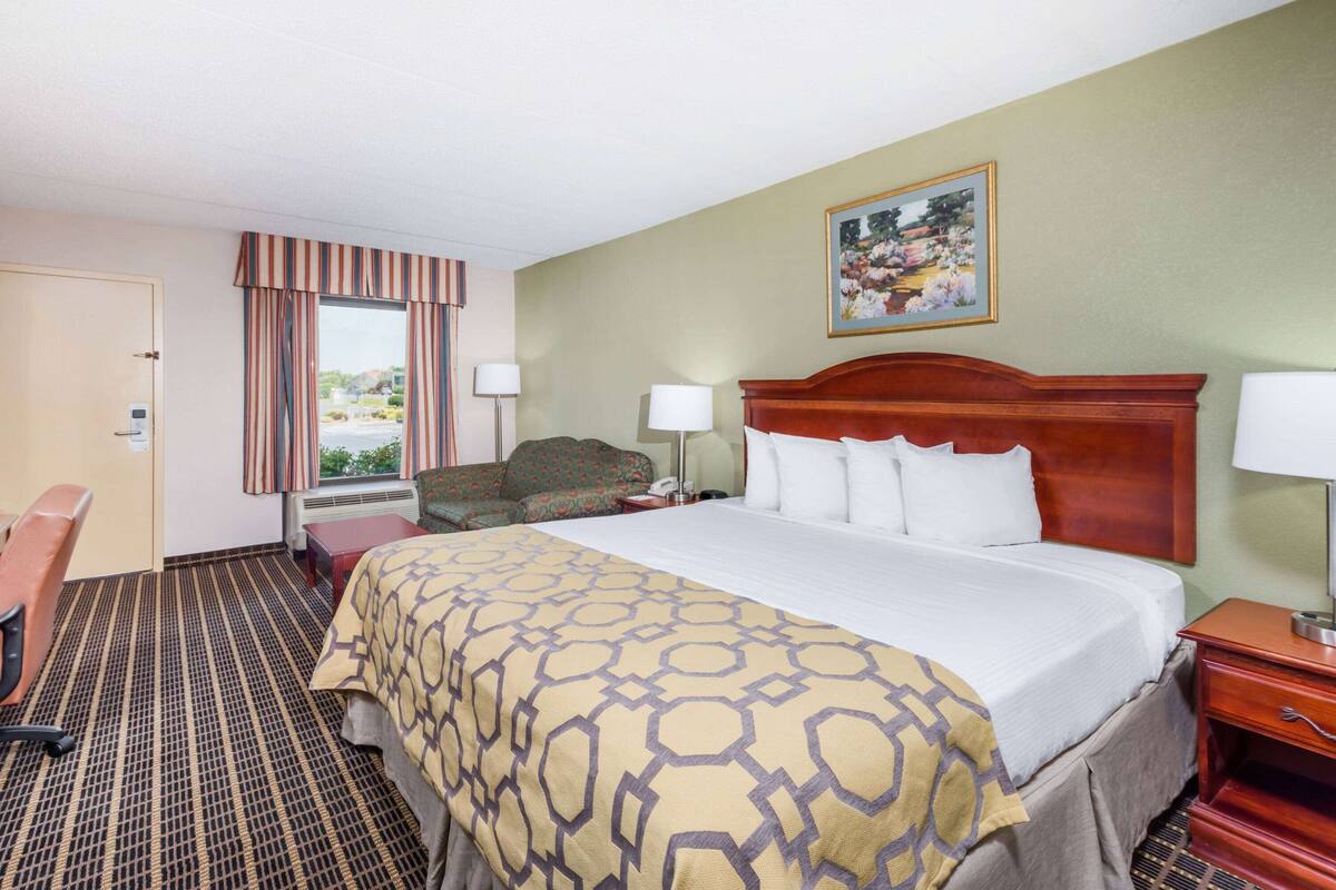 Une chambre d’hôtel avec un grand lit, un bureau, une chaise et une fenêtre avec des rideaux.