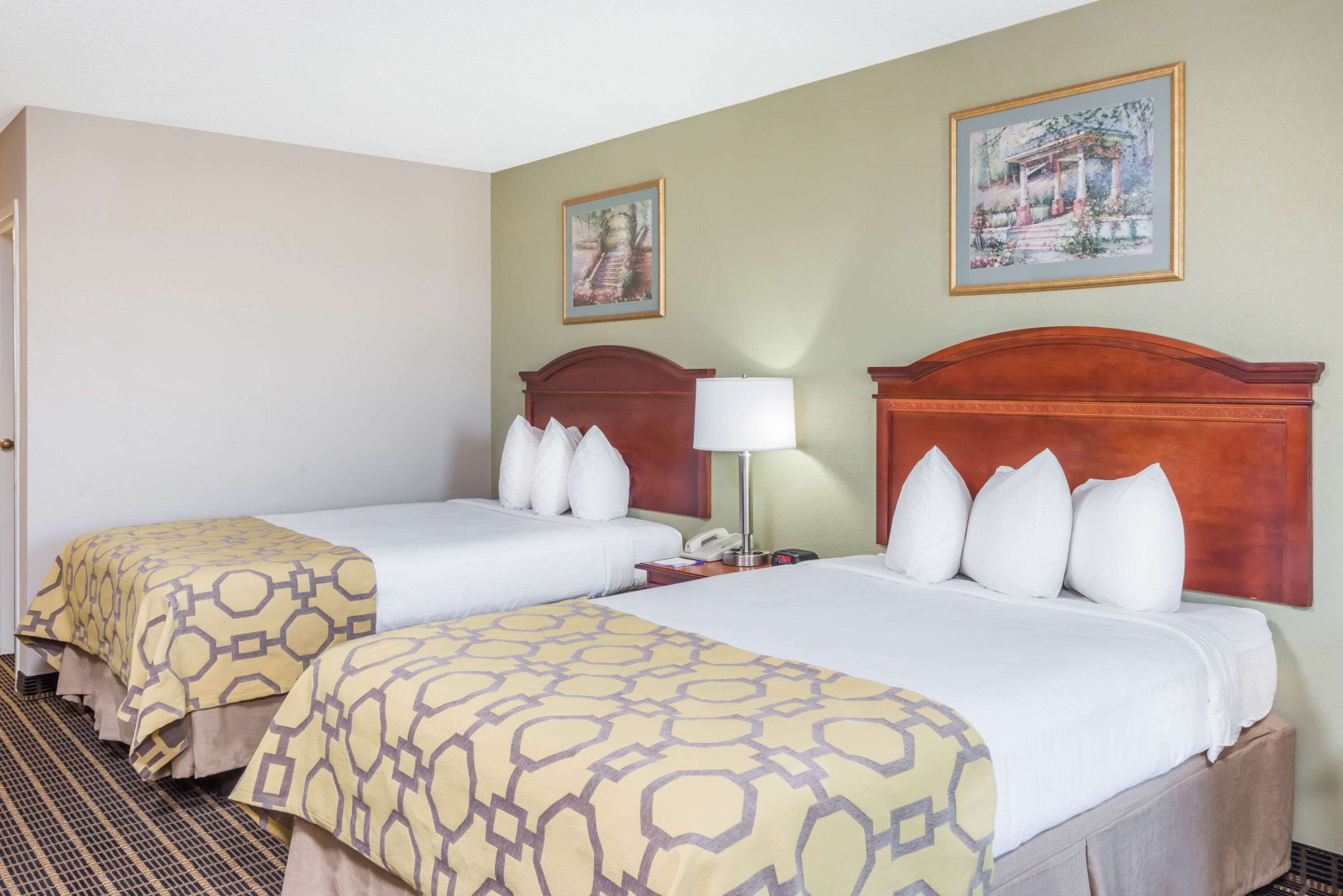 Habitación de hotel con dos camas, cada una con una colcha estampada, un cabecero de madera y una mesita de noche con lámpara.