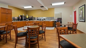 A dining area with wooden chairs and tables, a kitchen with appliances and a coffee machine, and a red door. - Best Western Paris Inn (Paris)