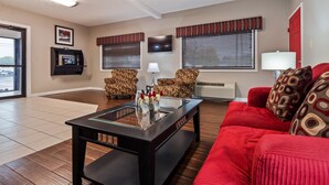 A living room with a red sofa, patterned armchairs, a glass-top coffee table, a flat-screen TV, and a fireplace. - Best Western Paris Inn (Paris)