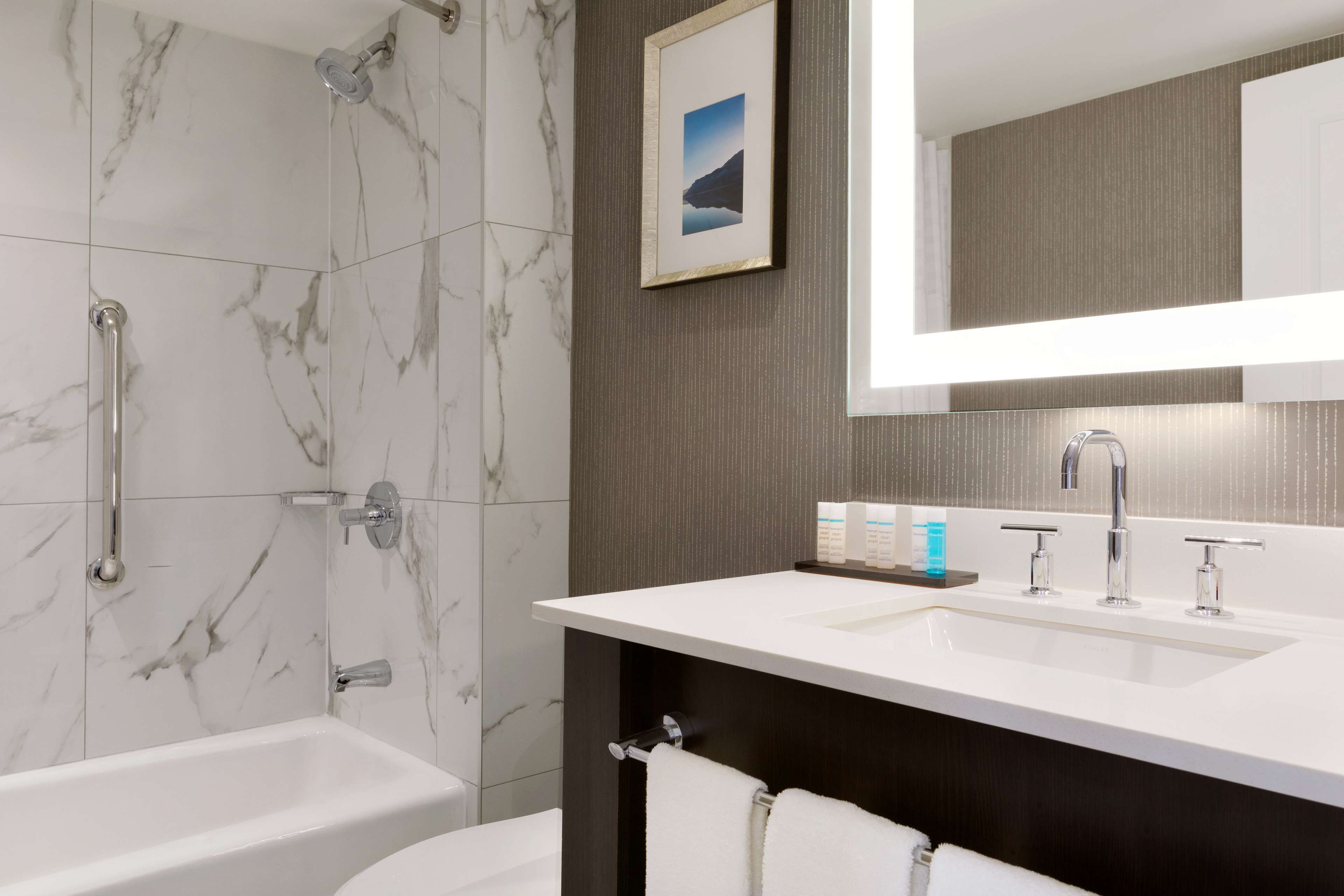 A modern bathroom with a marble shower, a large mirror, and a white sink with a dark countertop.