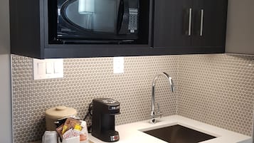 A compact kitchenette with a microwave, coffee maker, and sink.