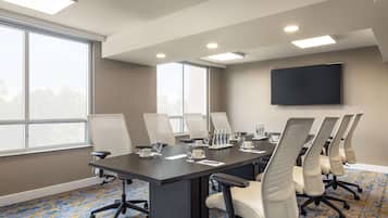 Un salón de conferencias con una gran mesa, varias sillas, un televisor de pantalla plana y amplias ventanas.