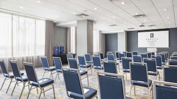 A conference room with rows of blue chairs, a projector screen, and a carpeted floor.