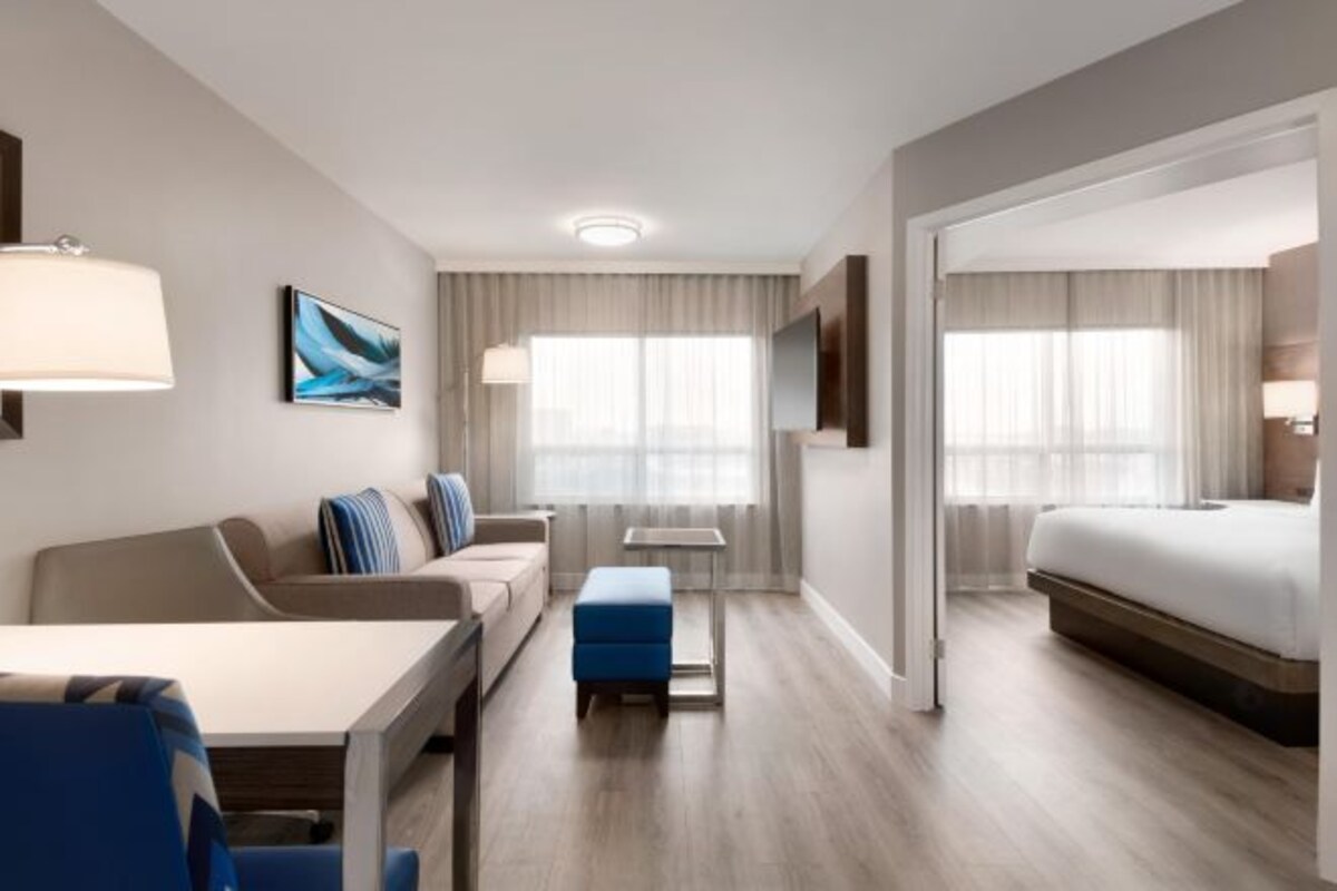 Ett modernt hotellrum med en soffa, ett litet bord, en blå pall, en säng och en tv.