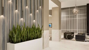 A modern lobby with a striped wall, a large planter with green plants, a chandelier, and two sofas. - Embassy Suites by Hilton Toronto Airport (Toronto)
