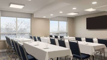 A conference room with tables, chairs, and a large screen.