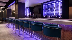 A bar area with a long counter, multiple stools, and a display of bottles and glasses. - Embassy Suites by Hilton Toronto Airport (Toronto)
