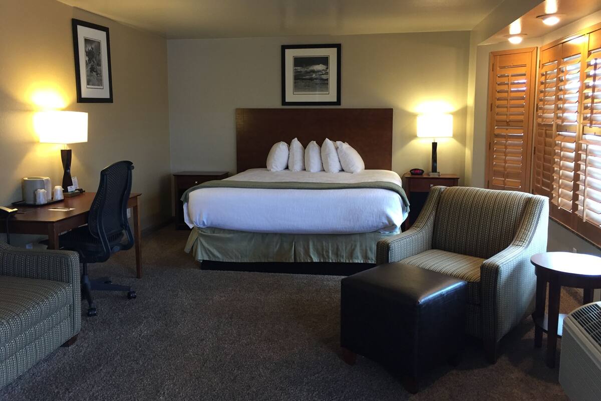 A hotel room with a large bed, two bedside tables with lamps, a chair, a small table, and a sofa.