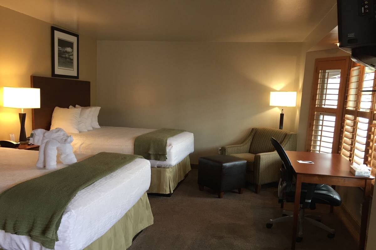 A hotel room with two beds, a desk, a chair, and a television.
