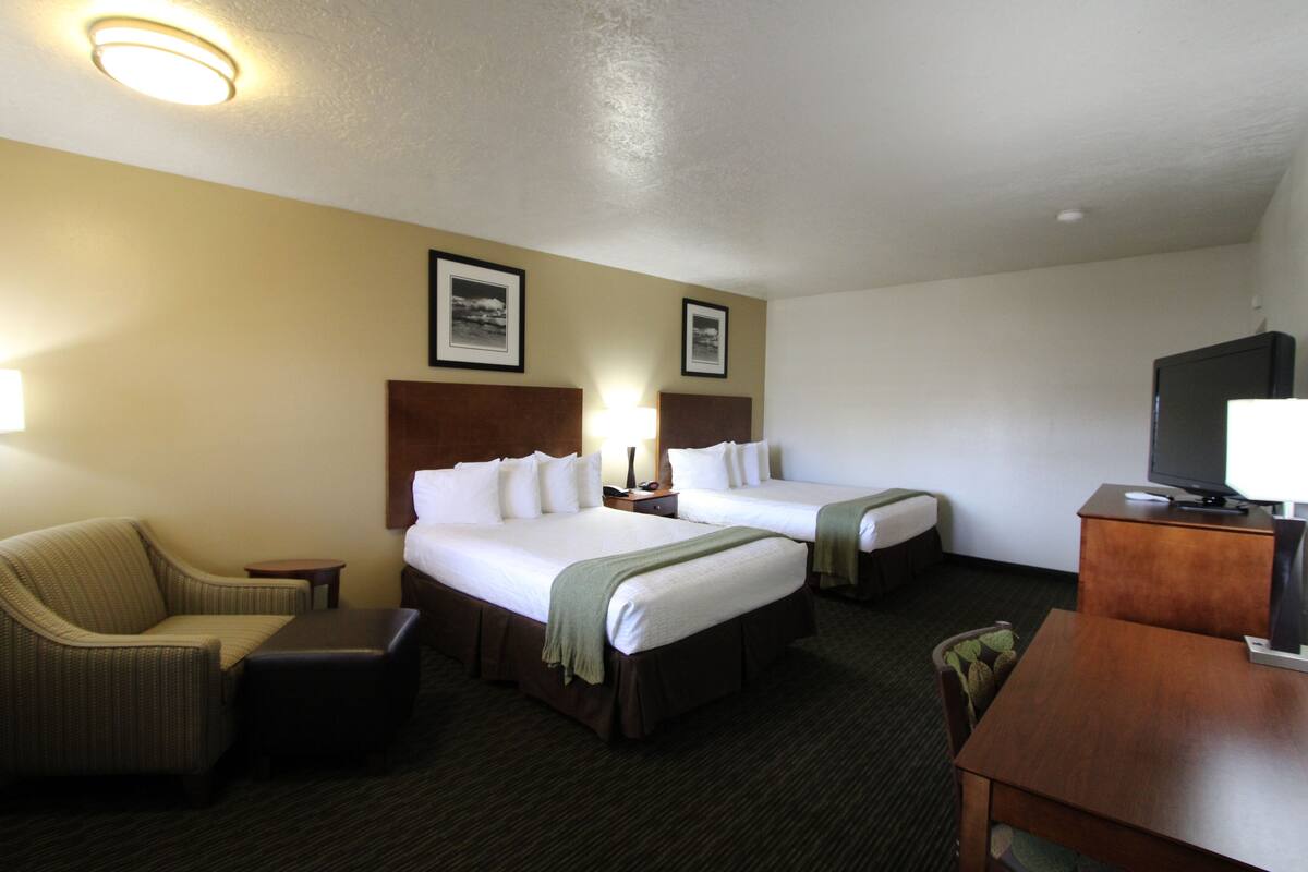 A hotel room with two beds, a sofa, a desk, and a television.