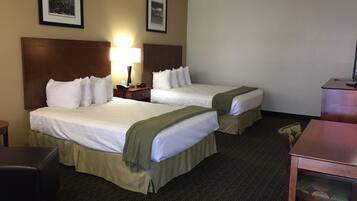 A hotel room with two beds, a desk, a chair, and a lamp.