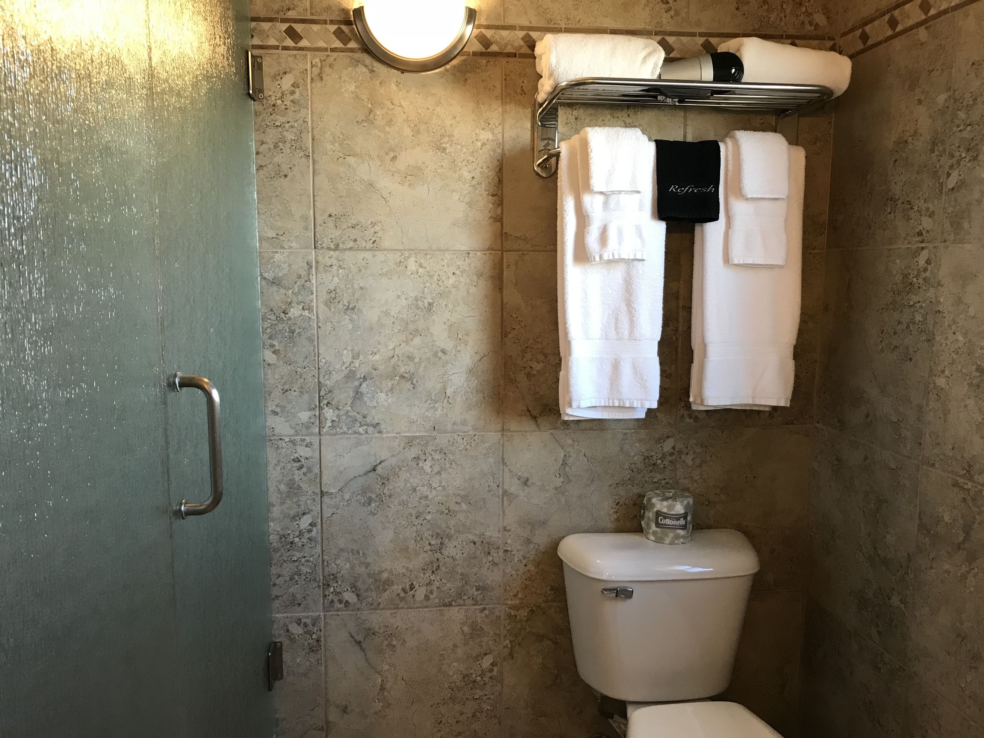 Une salle de bain comprenant des toilettes, un porte-serviettes avec des serviettes blanches et un espace douche.