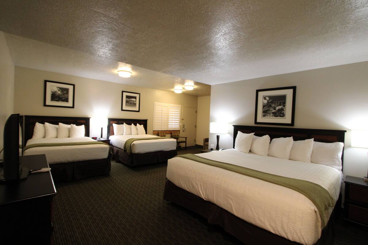 A hotel room with two beds, a desk, and a chair. There are framed pictures on the walls and a window with blinds.