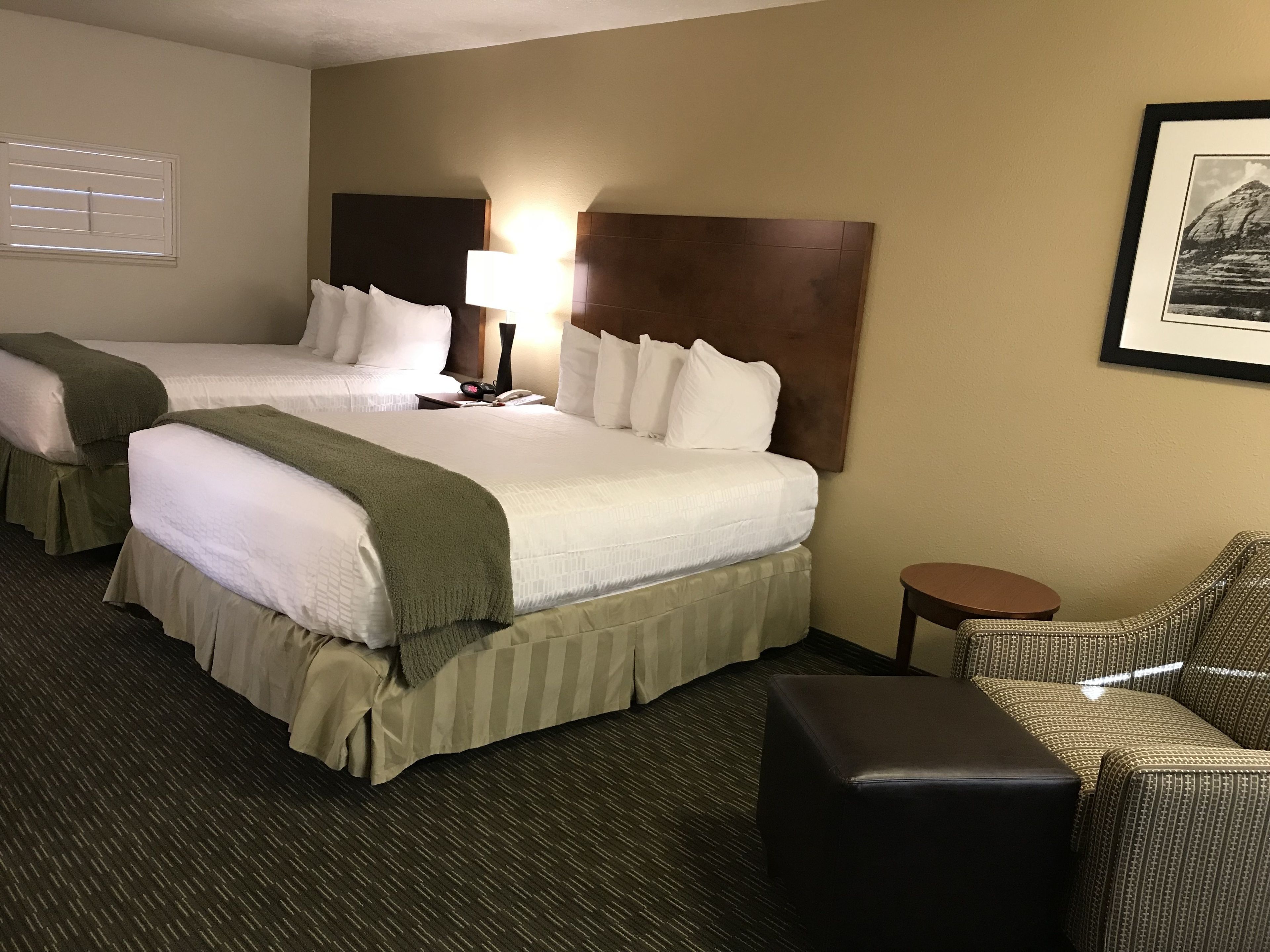 A hotel room with two beds, a nightstand, a lamp, a framed picture on the wall, and a small table.