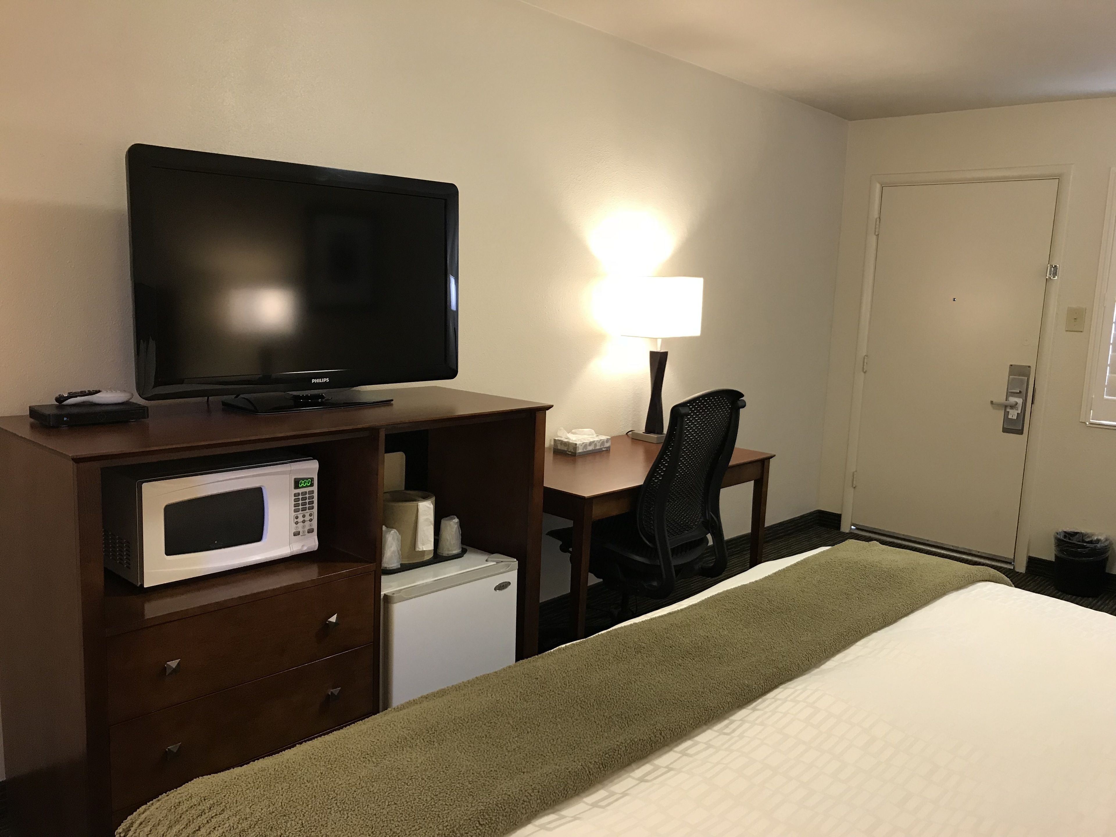 Une chambre d’hôtel comprenant un lit, un bureau avec une télévision, un four à micro-ondes, une chaise et une porte.