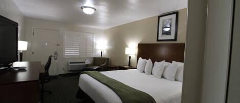 A hotel room with a bed, desk, chair, TV, and lamps.