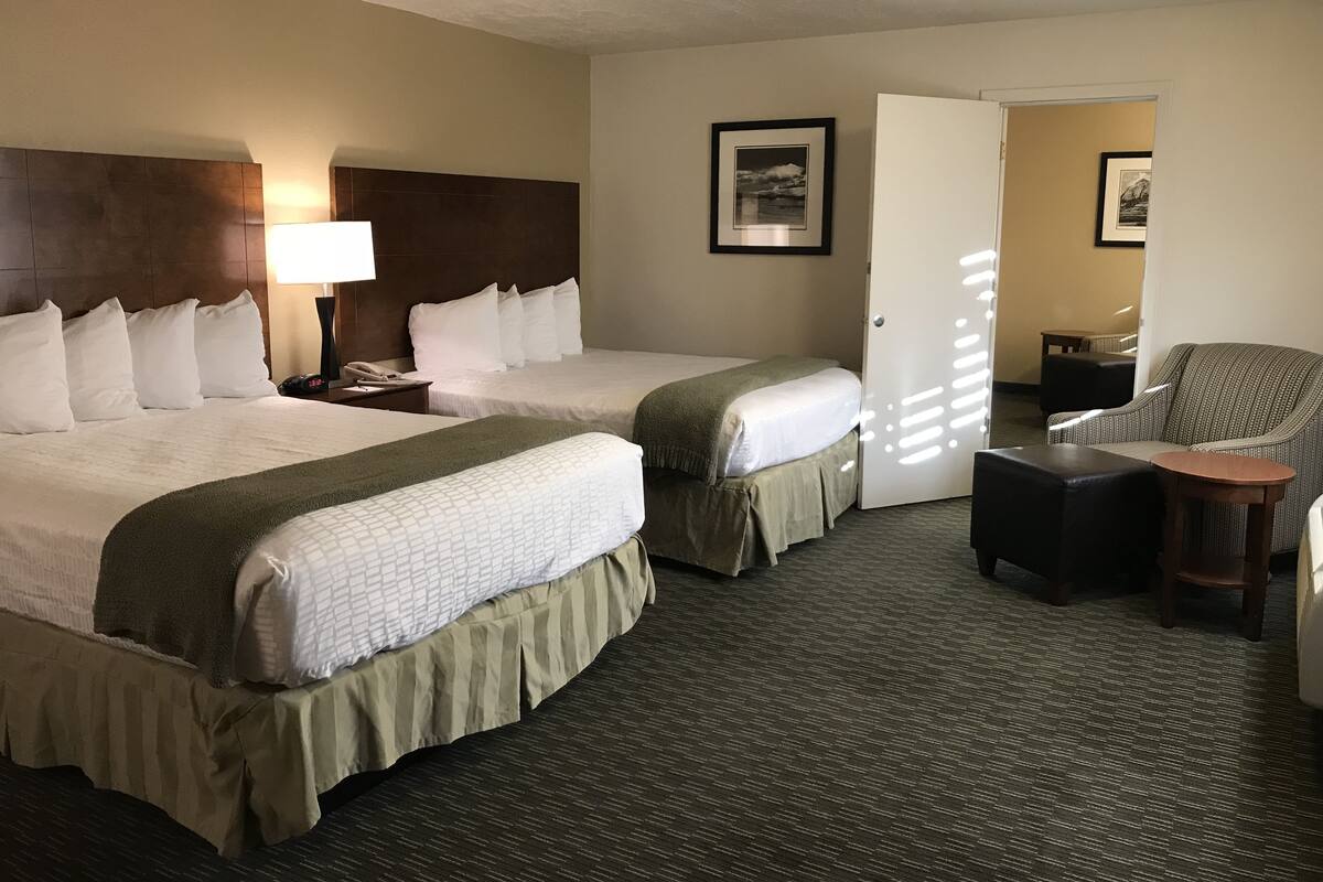 A hotel room with two beds, a desk, a chair, and a small table.