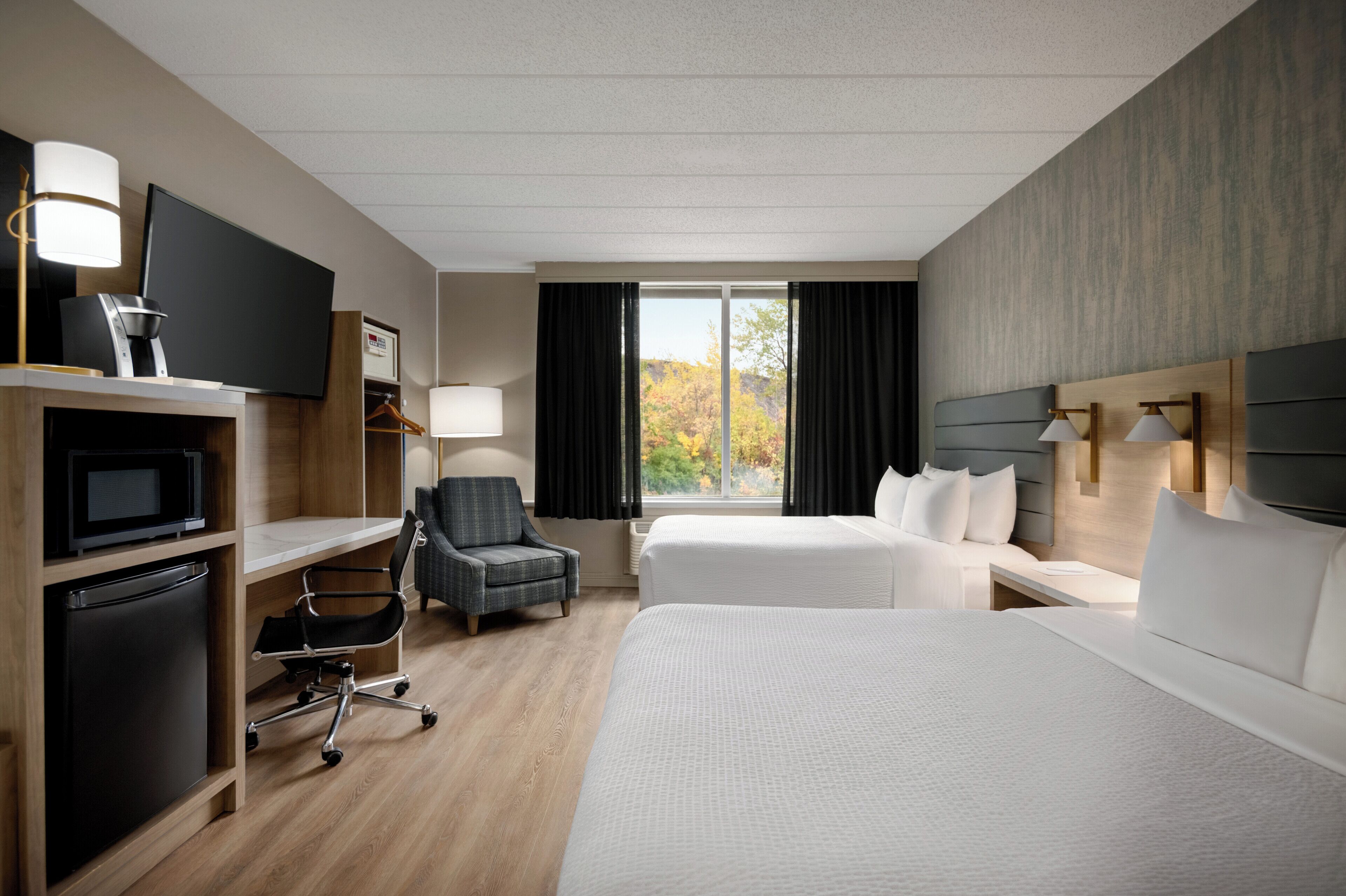 A hotel room with a large bed, a desk with a computer, a chair, a TV, and a window with curtains.