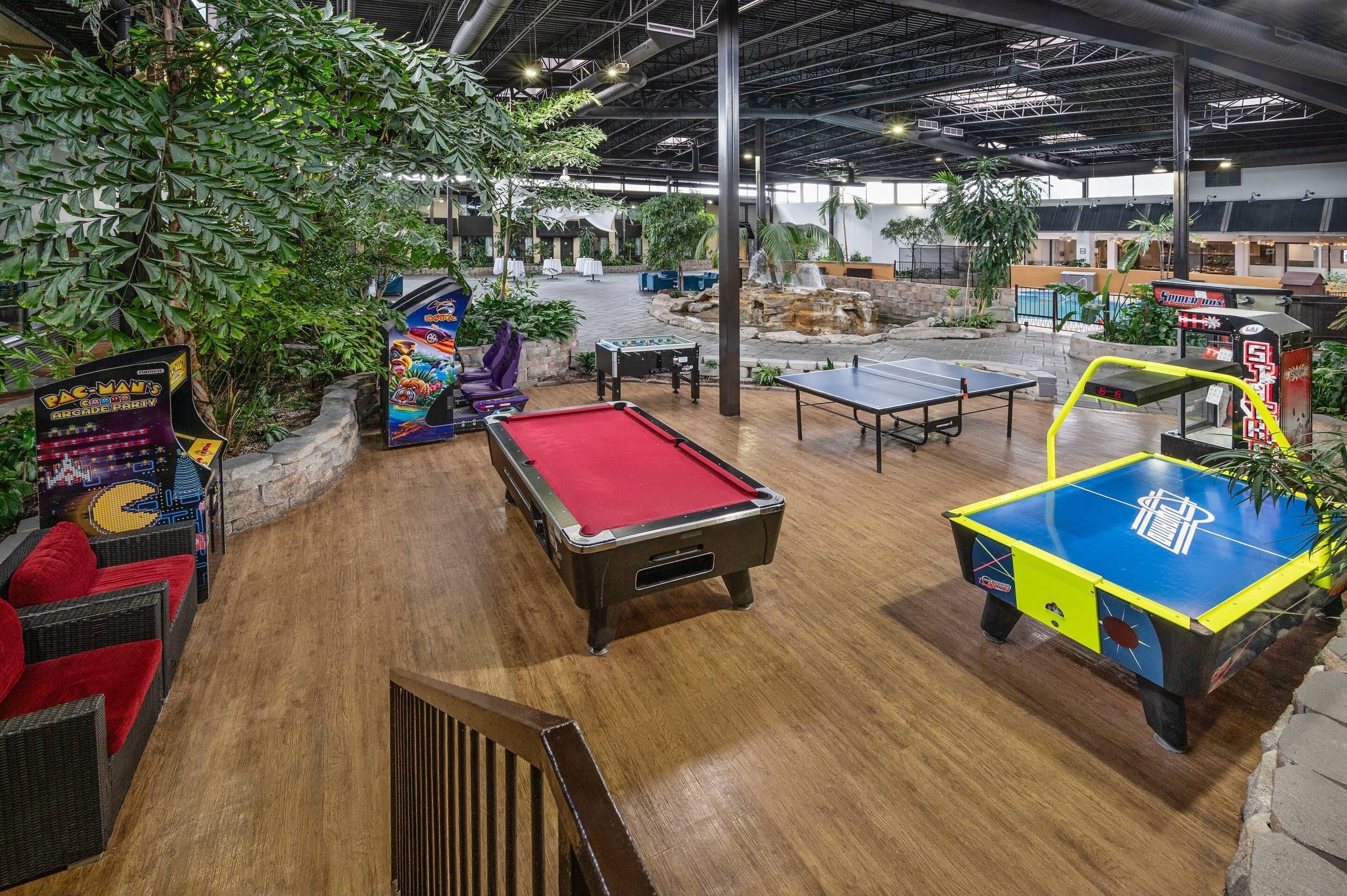 Un espace de loisirs intérieur comprenant des tables de billard, une table de ping-pong et des jeux d’arcade.