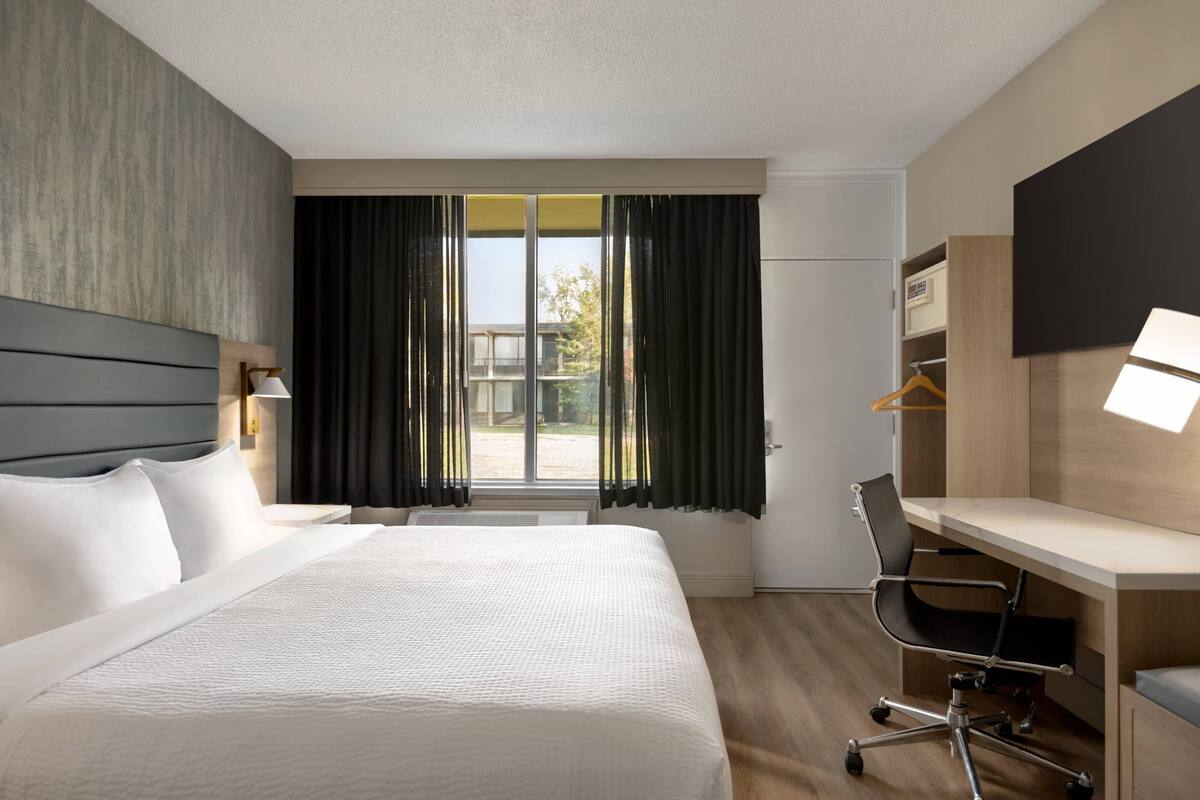Habitación de hotel con una cama grande, un escritorio, una silla, un televisor y una ventana con cortinas.