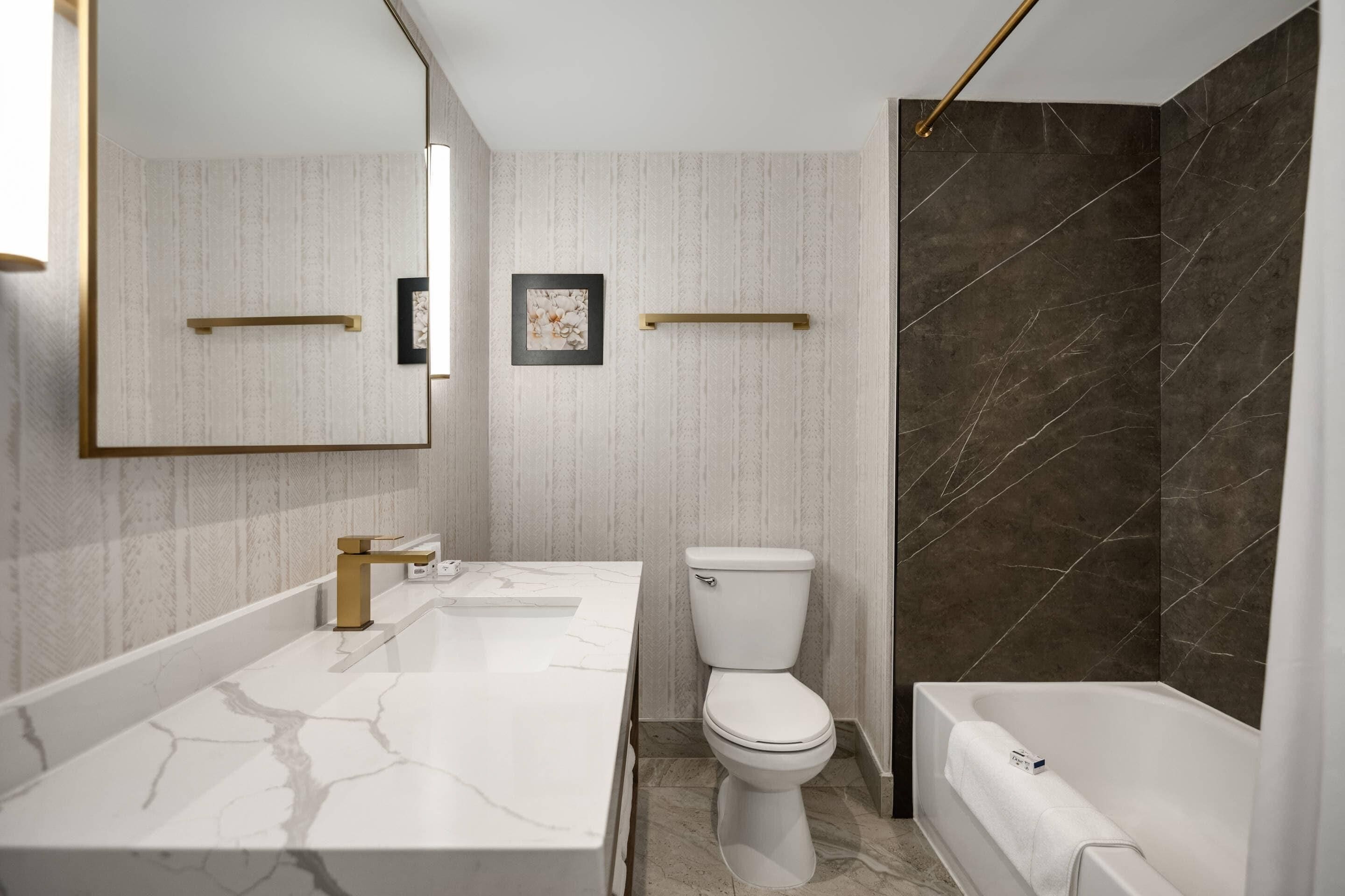 A modern bathroom with a marble vanity, a toilet, and a bathtub.