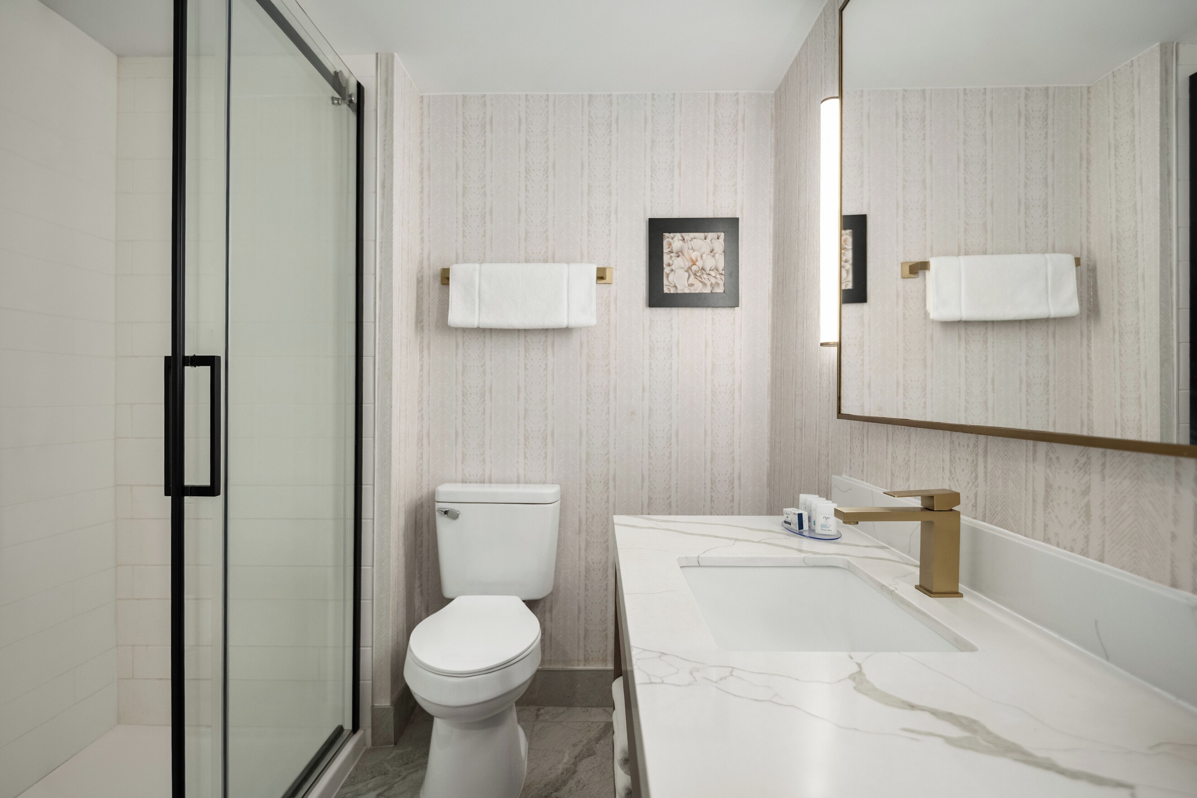 A modern bathroom with a glass shower enclosure, a white toilet, a marble sink, and a large mirror.