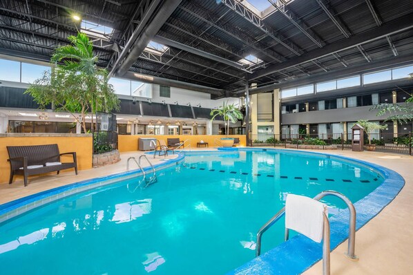 An indoor swimming pool with a clear blue water, surrounded by a poolside area with a bench and a towel rack.