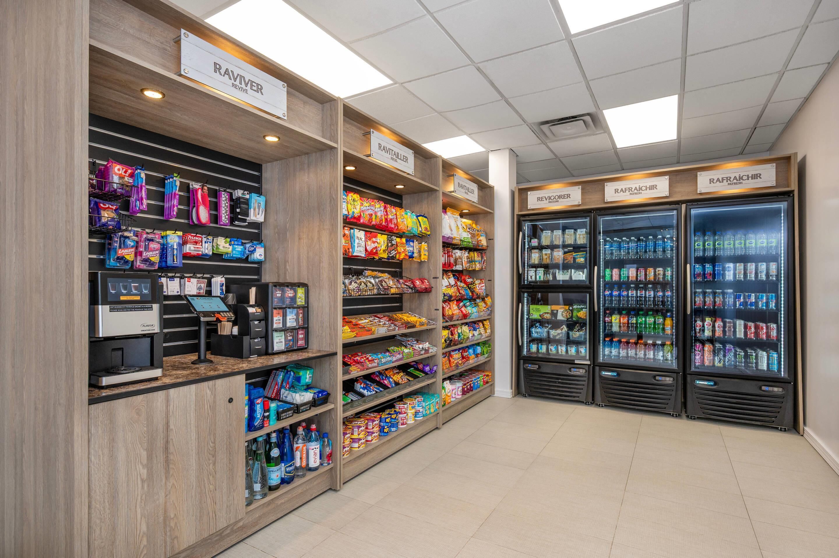 Une épicerie dont les rayons sont remplis d’en-cas et de boissons, équipée d’une caisse en libre-service et de distributeurs de boissons réfrigérés.
