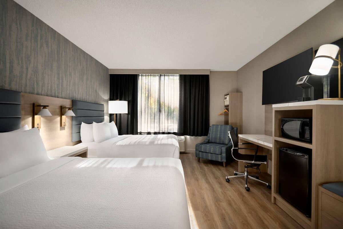 Habitación de hotel con dos camas, un escritorio, una silla, un televisor y un microondas.