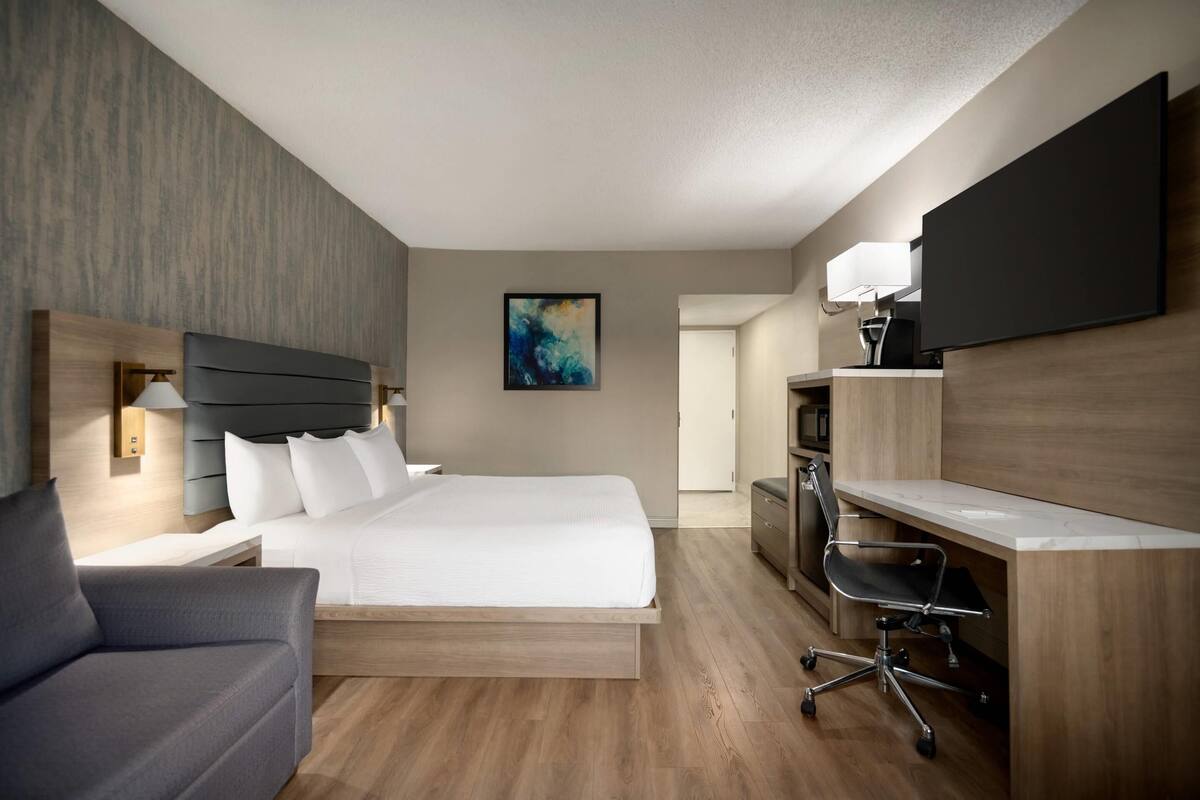 Una habitación de hotel moderna con una cama, un escritorio, una silla y un espejo grande.