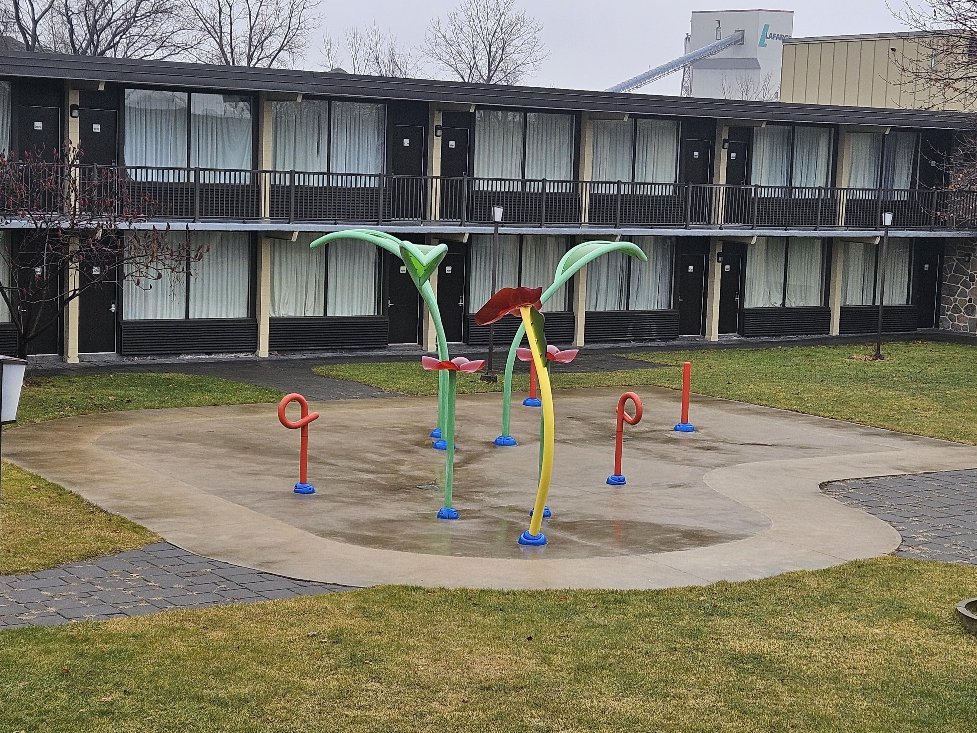 Un parque infantil con juegos de colores frente a un edificio de varias ventanas y balcón.