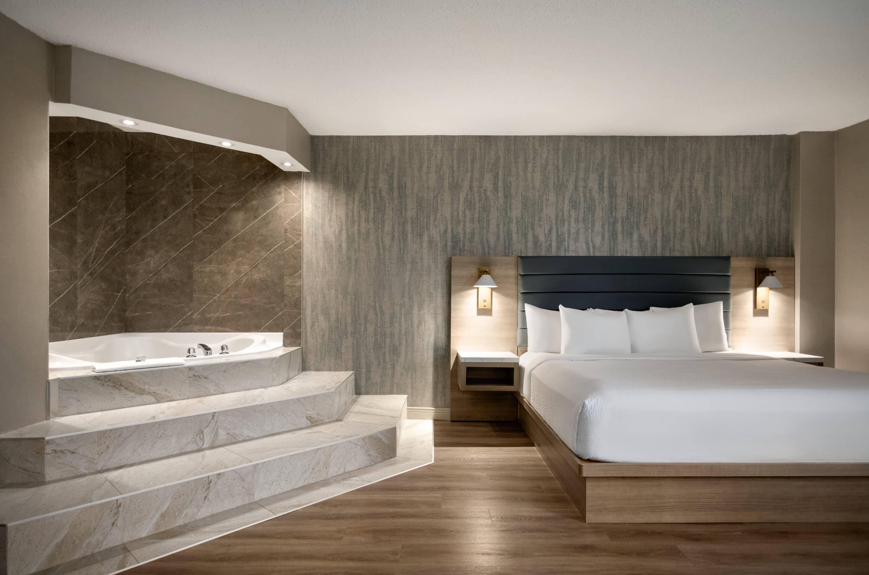 Una habitación de hotel moderna con baño de mármol, una cama grande y suelo de madera.