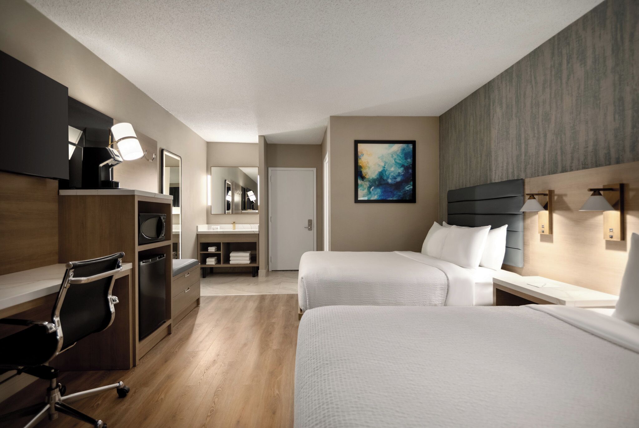 A hotel room with two beds, a desk, a chair, a microwave, and a bathroom.