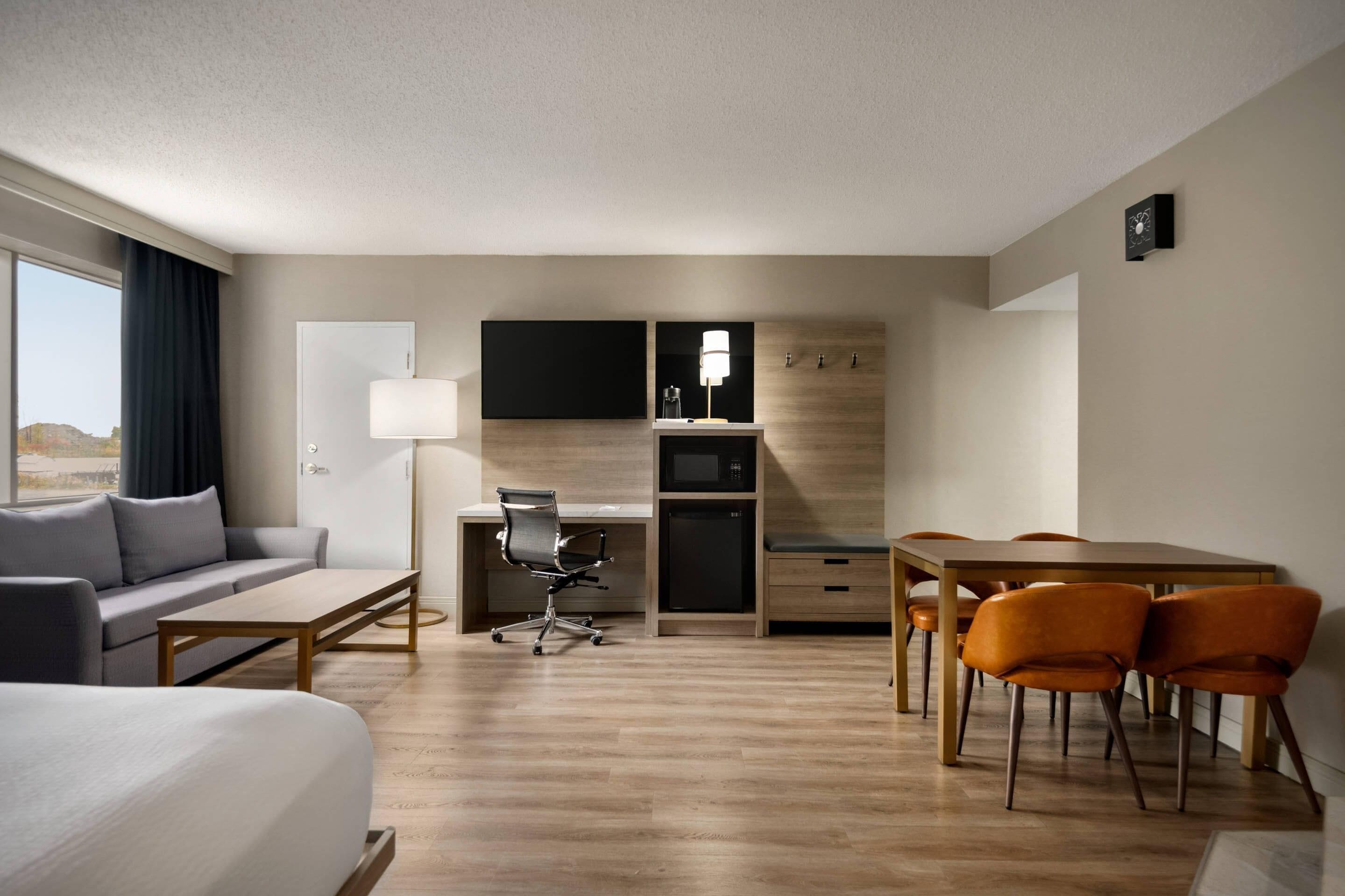 Habitación de hotel moderna con cama, sofá, escritorio, silla, mesa de comedor con sillas, televisor de pantalla plana y microondas.