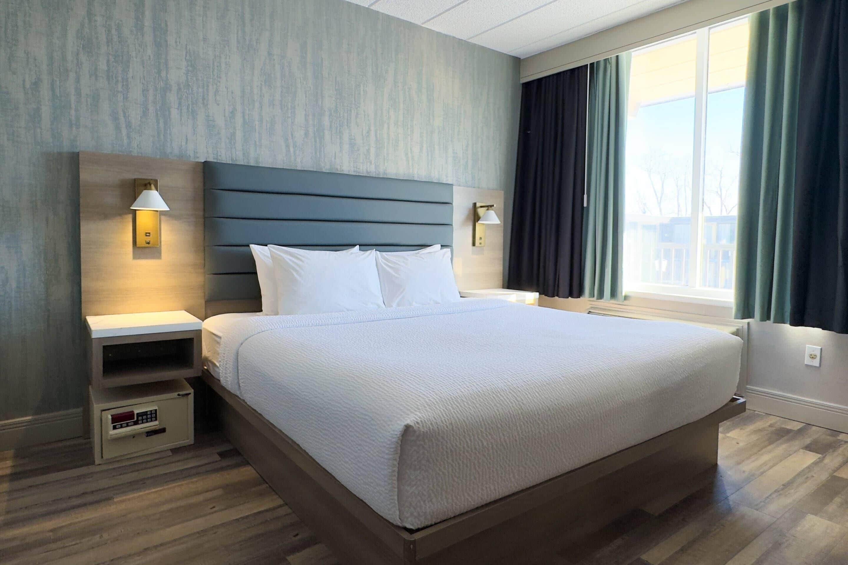 Ein Hotelzimmer mit einem großen Bett, zwei Nachttischen mit Lampen, einem Beistelltisch und einem Fenster mit Vorhängen.