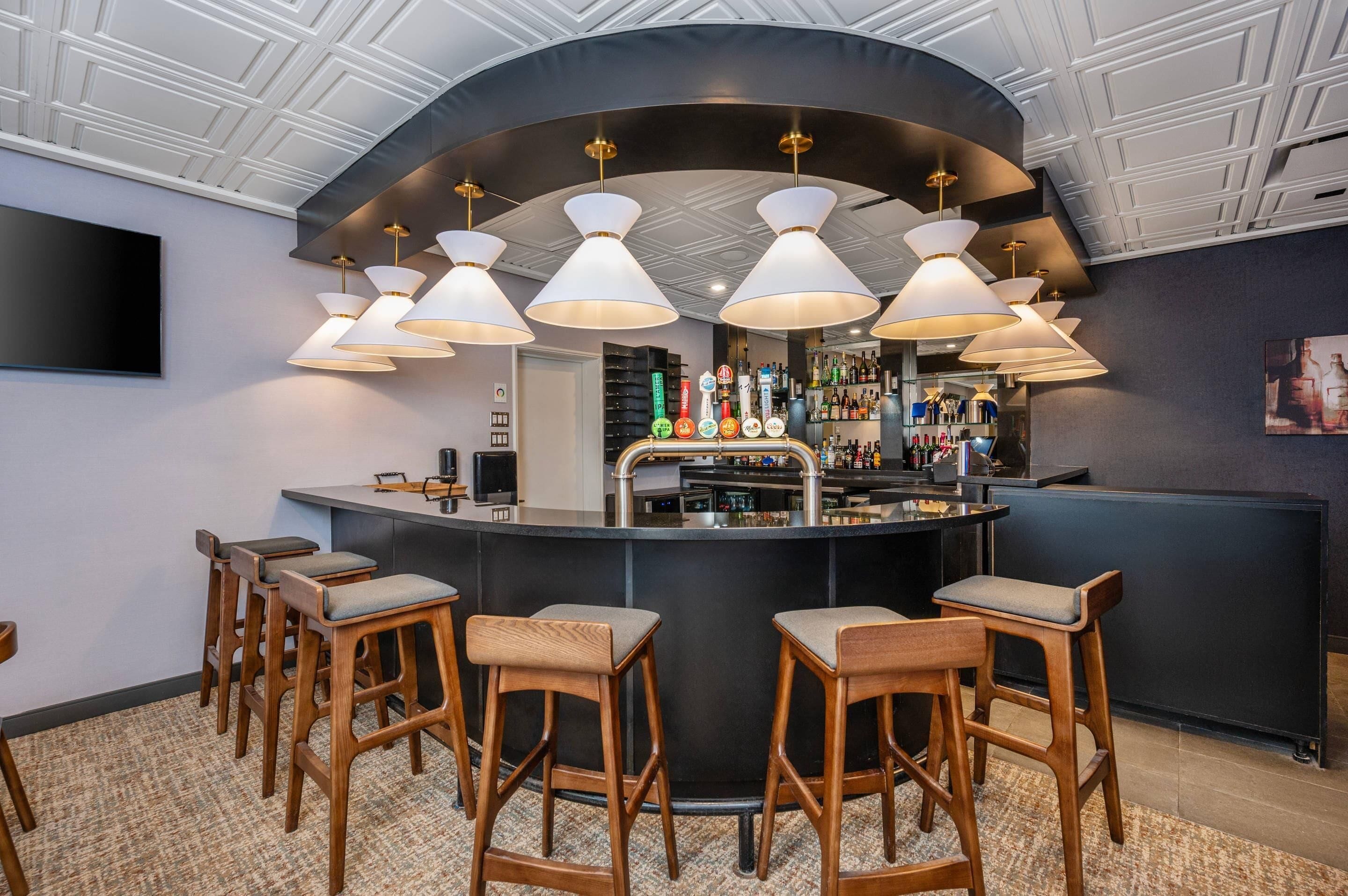 Uma área de bar com balcão curvo, vários bancos e luminárias pendentes.